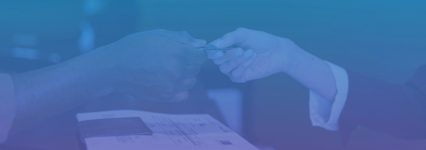 Two people exchanging a card across a desk with paperwork and a wallet in the foreground