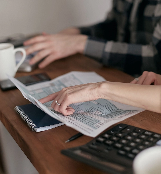Two people reviewing printed tax forms at a desk with a calculator and notebook