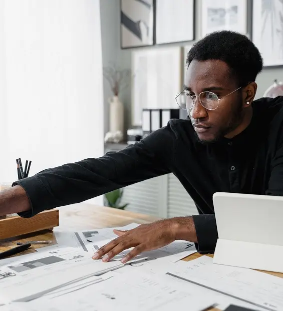 Person at a desk reviewing printed documents and charts beside a tablet